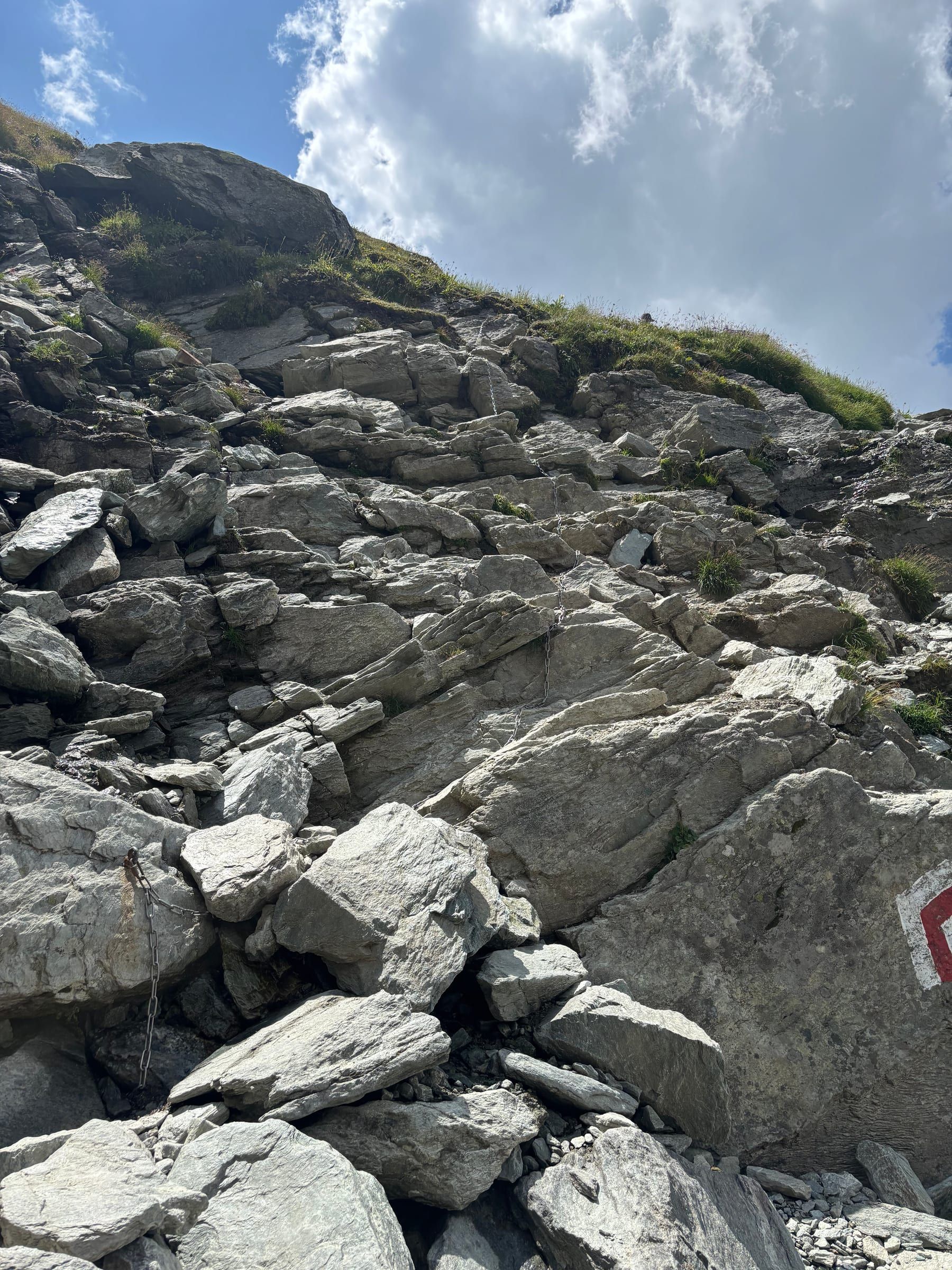 Mountain trail between large boulders, with the white-red-white waymark painted on a rock